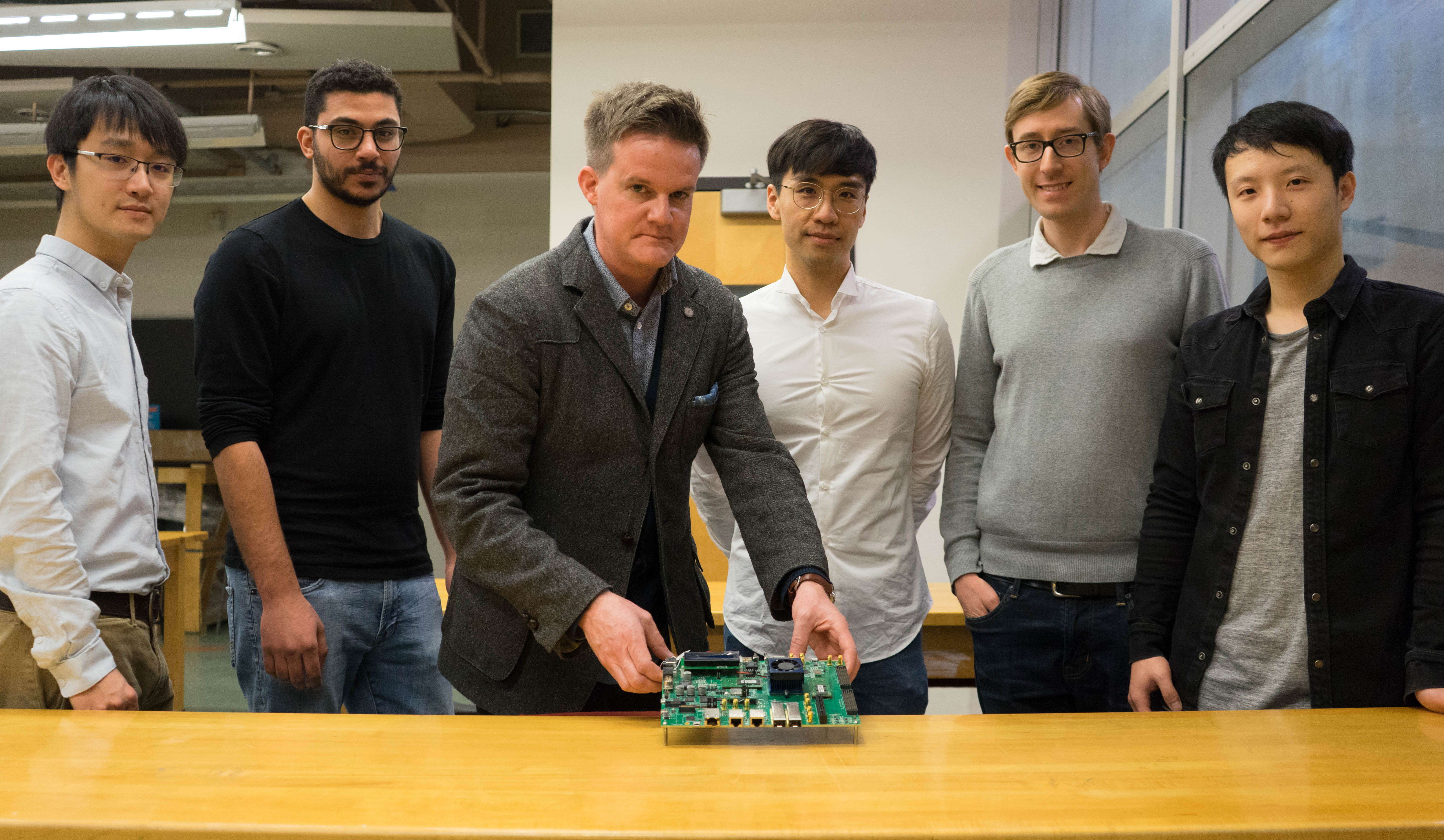 Professor Jason Anderson holds an FPGA board with the LegUp team behind him. Left to right, Zhi Li (CompE 1T3), Omar Ragheb (CompE MEng 1T8), Professor Jason Anderson (ECE), Dr. Jongsok Choi (CompE MASc 1T2, PhD 1T6), Dr. Andrew Canis (CompE PhD 1T5), and Ruolong Lian (CompE 1T3, MASc 1T6) are making it easier for software developers to leverage servers based on FPGAs. (Photo: Jessica MacInnis)