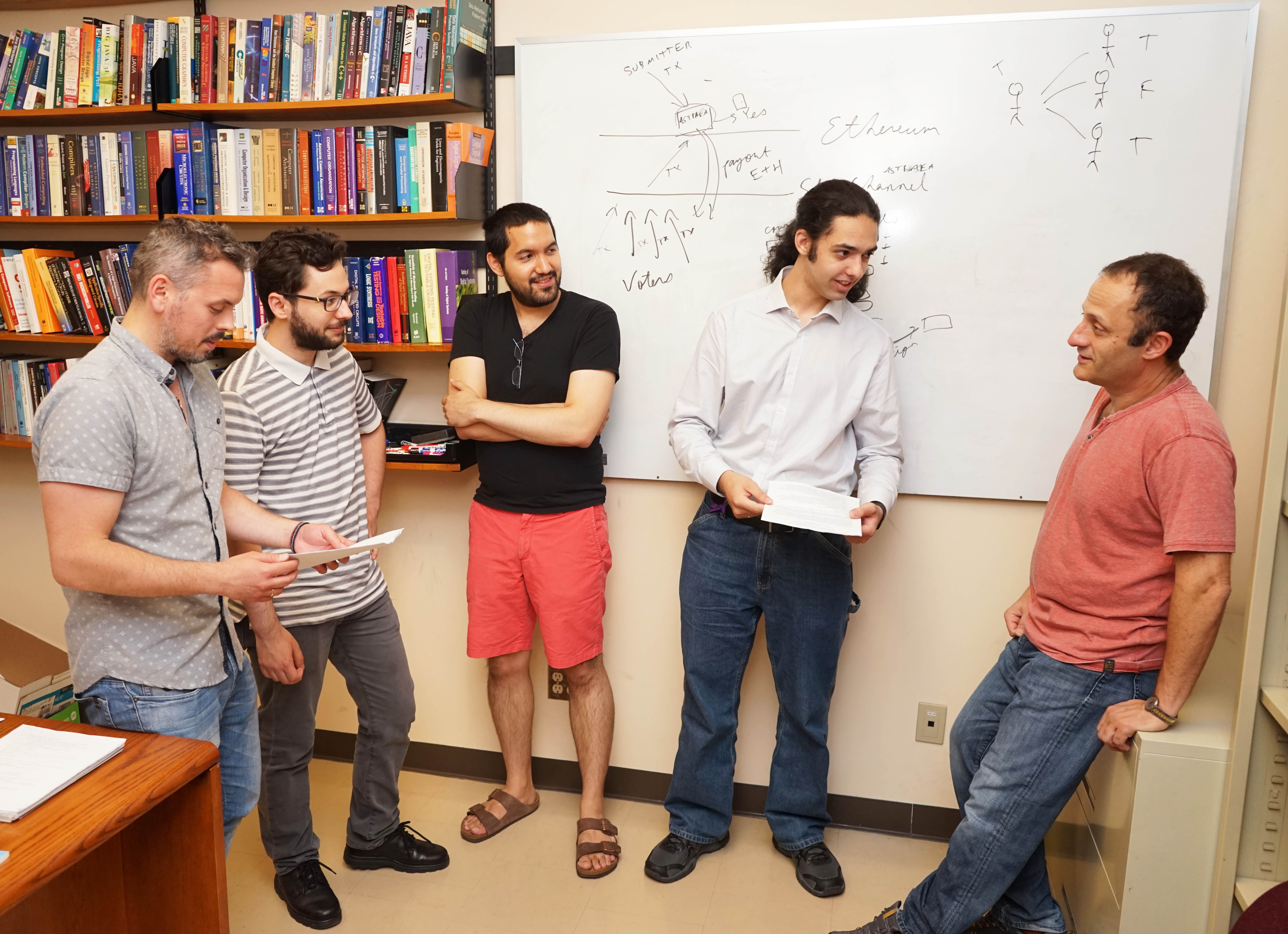 Professor Veneris stands with graduate students at a whiteboard.