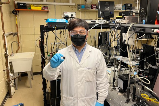 Researcher in lab coat holding small cell between fingers