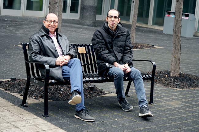 Two men sitting on metal bench in a courtyard