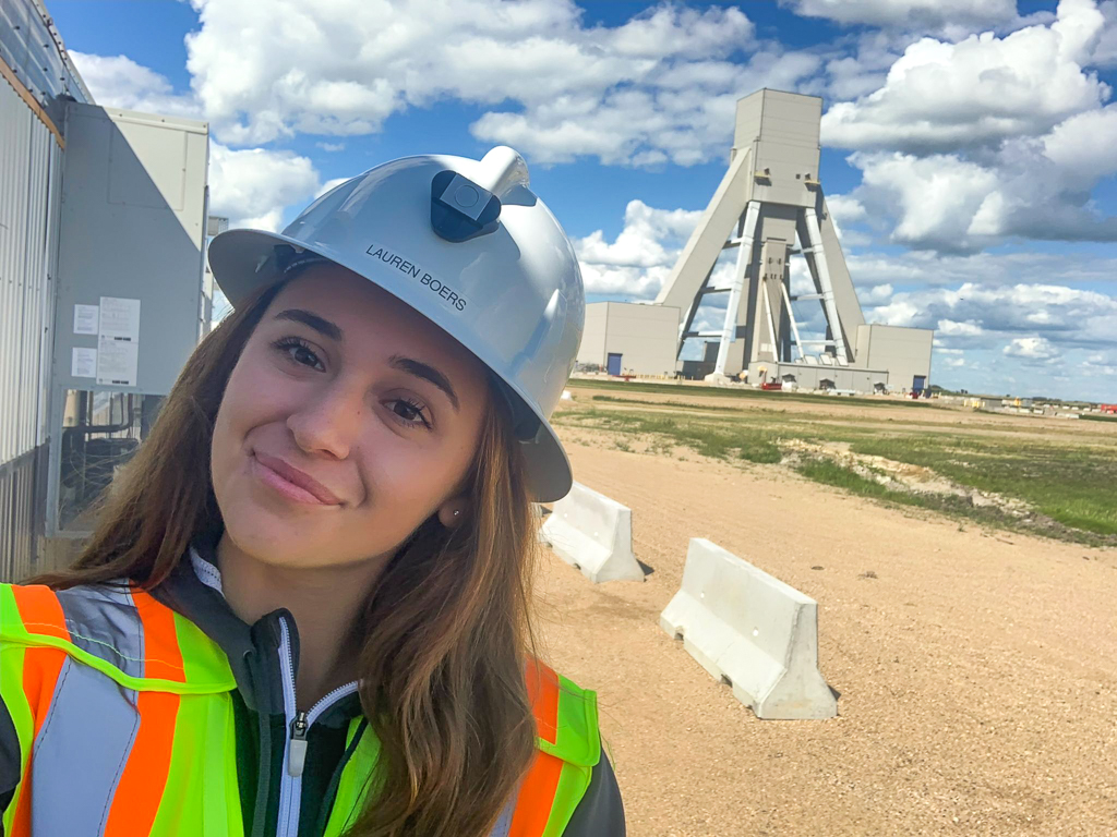 Woman in hardhat against backdrop with machinery