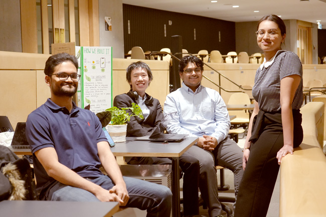Four students posed around project board and plants on a table