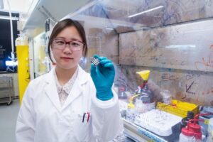 Researcher in lab coat with solar cell pinched between fingers