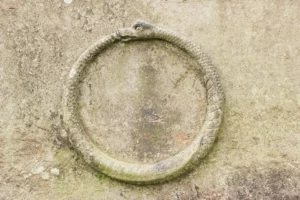 A stone ouroboros is centred with a stone background.