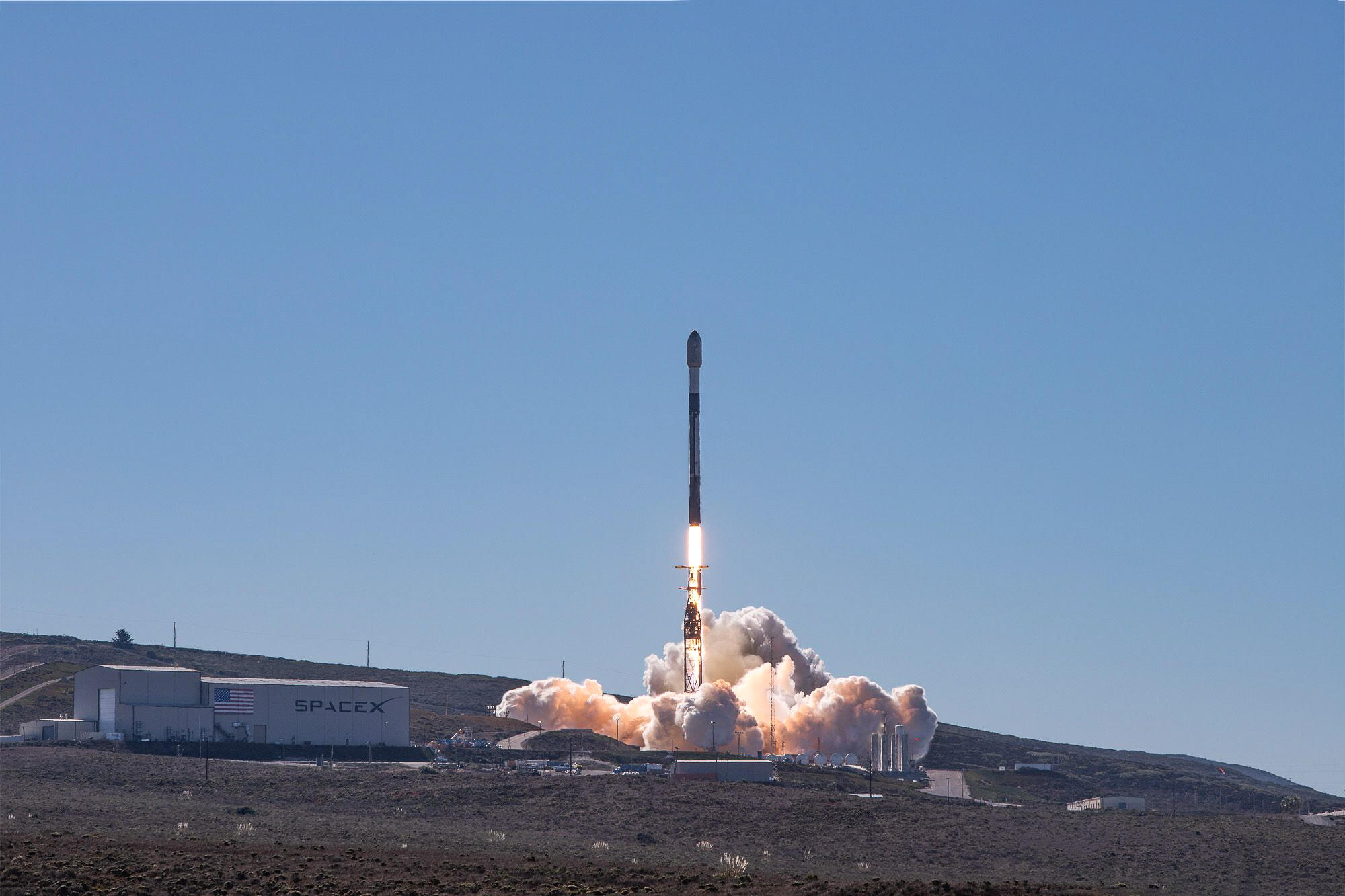 Rocket at moment of launch, with flames and smoke against a brilliant blue sky