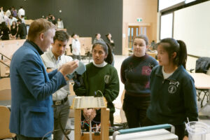 Professor gestures to students standing around him near the setup for their project